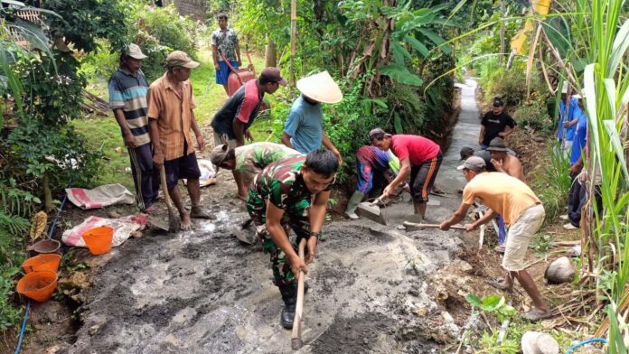 Babinsa Bantur Serka Hadi Sunarko membantu warga Dusun Durmo dalam kegiatan kerja bakti pengecoran jalan