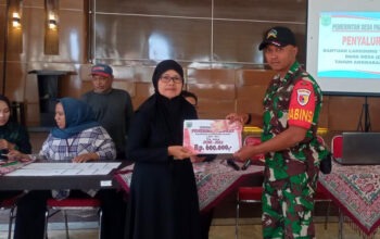 Babinsa Pandanrejo berpakaian dinas loreng TNI dengan ramah menyerahkan "Bantuan Langsung Tunai Dana Desa" kepada seorang warga desa KPM.
