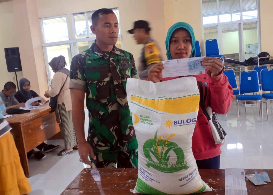 Babinsa Sumberbrantas, Serda Zarkasih, mendampingi penyaluran bantuan beras di Balai Desa Sumberbrantas.