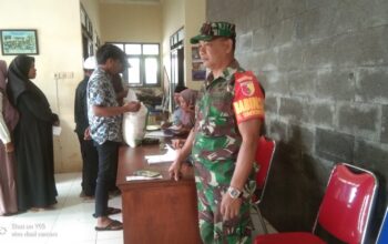 "Seorang Babinsa Sumberkerto memantau distribusi bantuan beras di desa, menjaga keamanan dan ketertiban selama proses."
